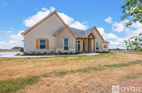 A house with a brown roof and a white exterior is surrounded by a grassy field.