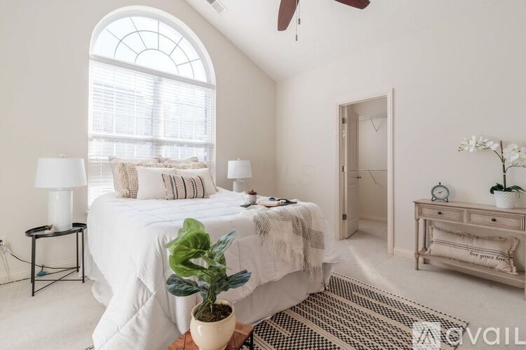 A bedroom with a large bed, a ceiling fan, and a window with blinds.