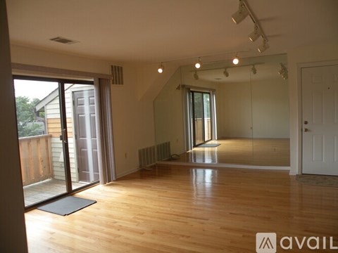 A spacious room with wooden floors and a sliding glass door leading to a balcony.