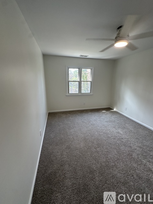 A room with a carpeted floor, a ceiling fan, and a window with a view of trees outside.