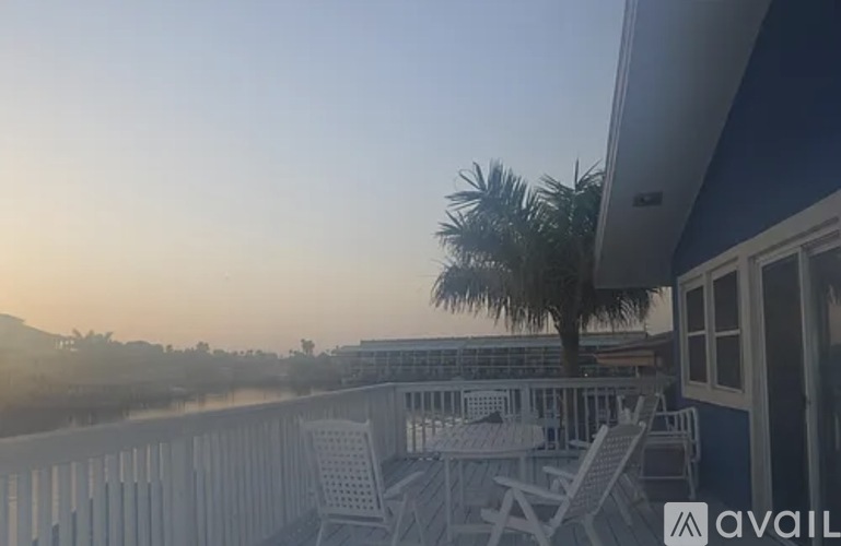 A balcony with chairs and a table overlooks a body of water with trees in the distance.