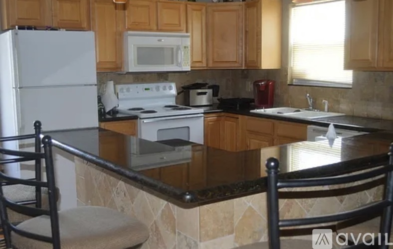 A kitchen with a white refrigerator, microwave, toaster, and a red kettle on a counter with a black chair.