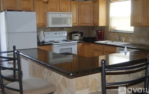 A kitchen with a white refrigerator, microwave, toaster, and a red kettle on a counter with a black chair.