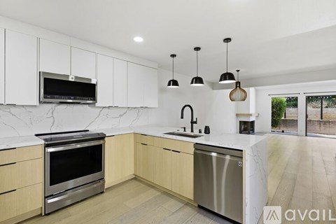 A modern kitchen with a stainless steel dishwasher and oven, white cabinets, and a marble countertop.