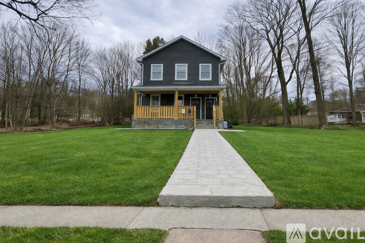 A house with a grey roof and a wooden deck is surrounded by a grassy lawn and trees.