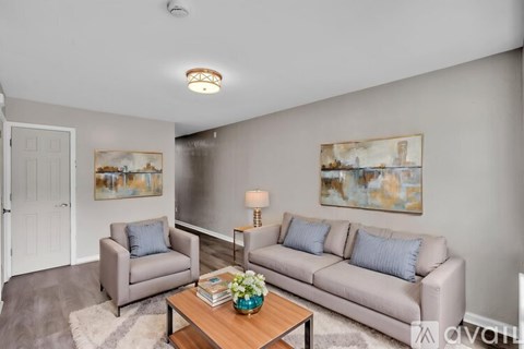 A living room with a grey couch, a grey armchair, a coffee table with a vase of flowers on it, and two paintings on the wall.