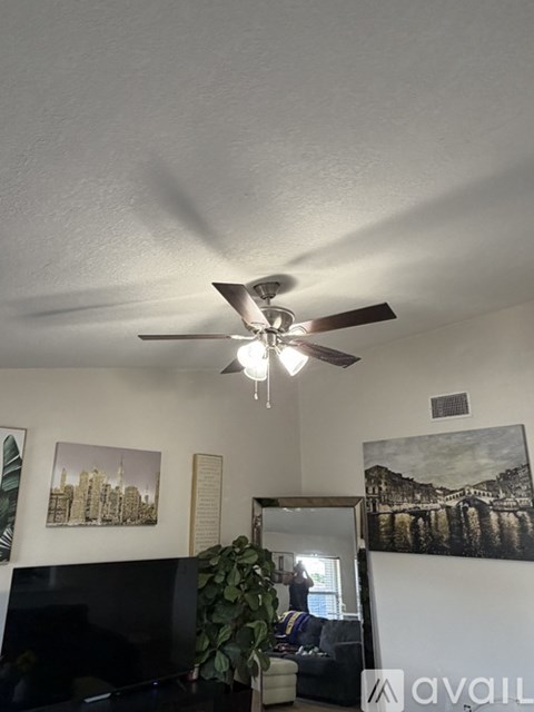 A living room with a ceiling fan and a painting of a cityscape on the wall.