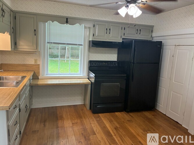 A kitchen with a black refrigerator and wooden floors.