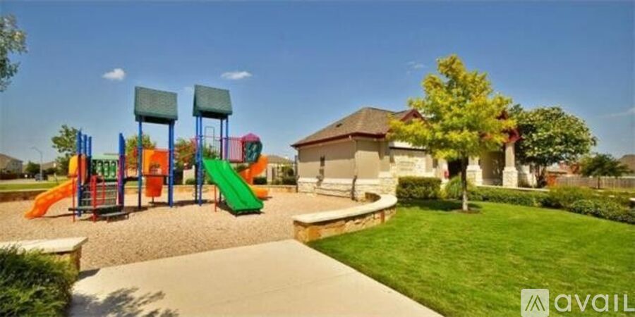 A playground with a slide, swings, and a tree in front of a building.