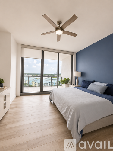A bedroom with a bed, a ceiling fan, and a view of the outside through the window.