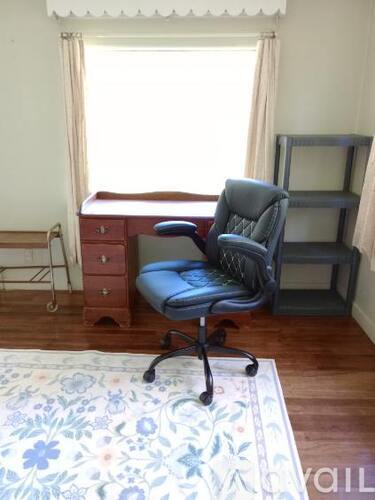 A blue chair is in front of a desk with a wooden chair and a wooden dresser in the background.