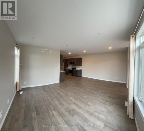 A spacious room with wooden flooring and a large window on the right side.