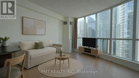 A living room with a couch, a coffee table, and a television with a city view through the windows.