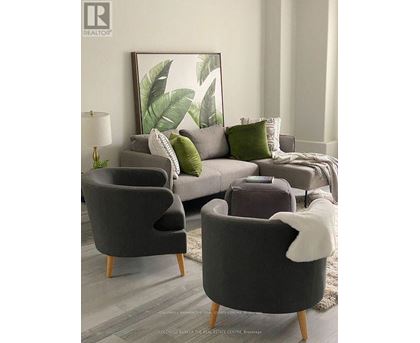 A living room with a grey couch, two grey armchairs, and a large leafy picture on the wall.