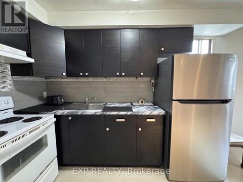 A kitchen with black cabinets and a stainless steel refrigerator.