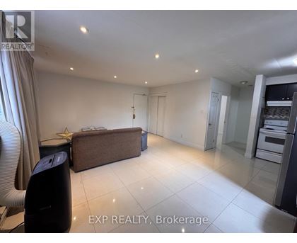 A spacious living room with a brown sofa and a kitchen area in the background.