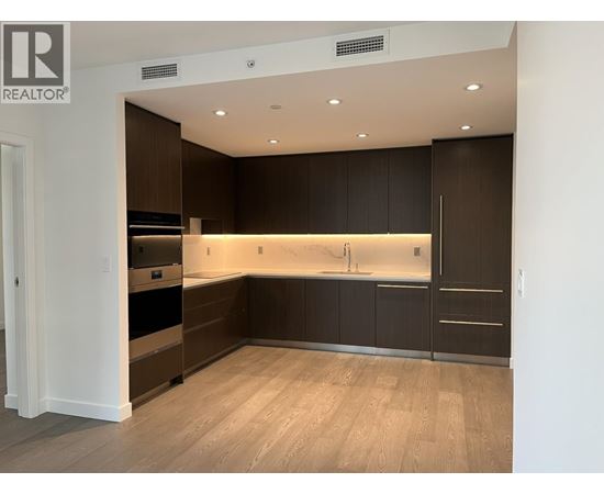 A modern kitchen with dark brown cabinets and a wooden floor.