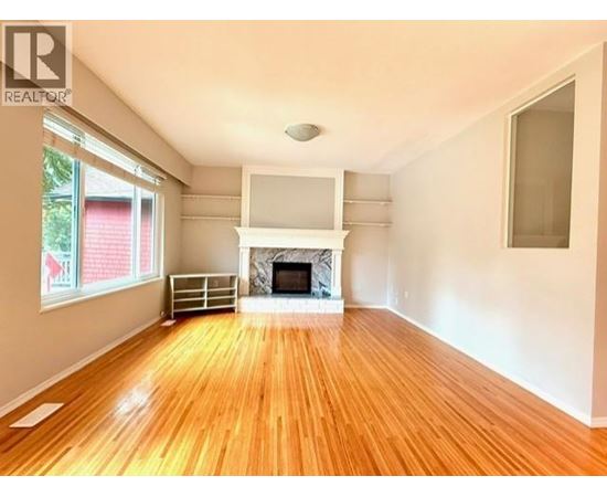 A large empty room with a fireplace and wooden floors.