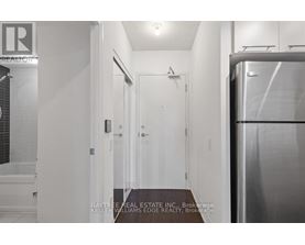 A hallway with a refrigerator on the right and a door on the left.