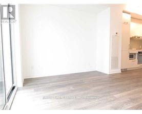 A large empty room with wooden flooring and a kitchen area in the background.