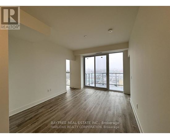 A spacious room with wooden flooring and sliding glass doors leading to a balcony.