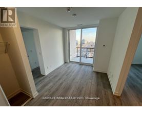 A spacious room with wooden flooring and a view of the city through the sliding glass door.