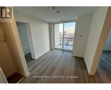 A spacious room with wooden flooring and a view of the city through the sliding glass door.