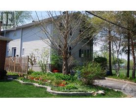 A house with a grey siding and a red door is surrounded by a garden with red flowers.