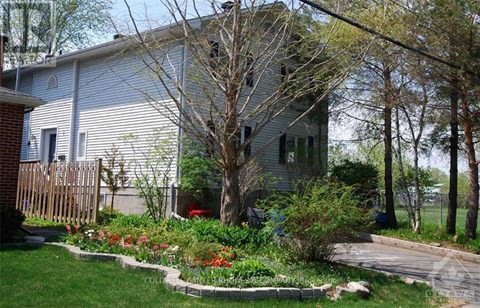 A house with a grey siding and a red door is surrounded by a garden with red flowers.