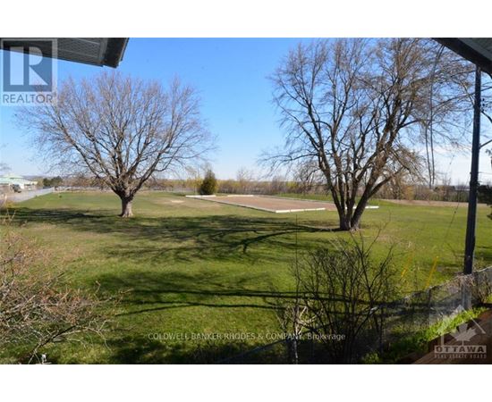A grassy field with two trees and a sign for Coldwell Banker Riggs & Company in the foreground.