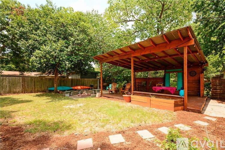 A wooden pavilion with a red roof is surrounded by a grassy area and trees.