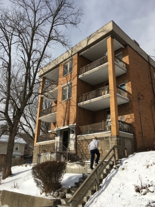 A man in a white shirt and black pants is walking up a snowy staircase in front of a red brick apartment building.