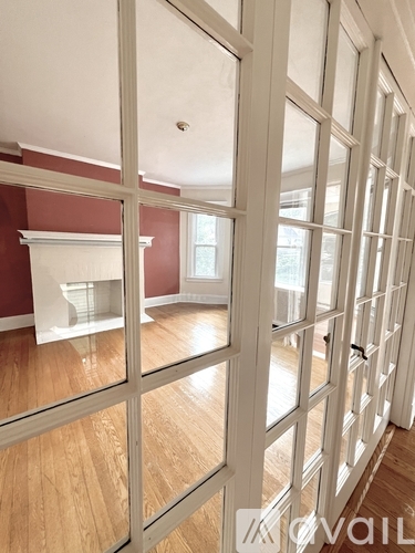 A room with a red wall and wooden flooring is visible through a glass door.
