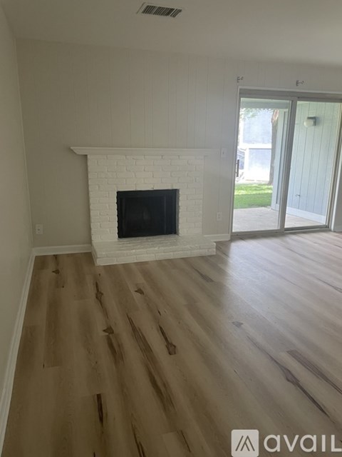 A white fireplace with a flat screen TV mounted above it in a room with wooden floors and a sliding glass door.