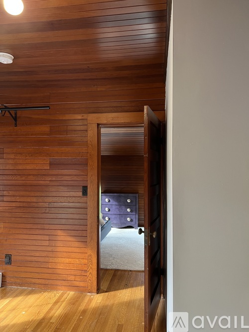 A room with a wooden wall and a door leading to a bedroom.