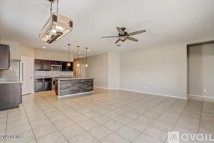 A spacious living room with a kitchen in the background and a fan on the ceiling.