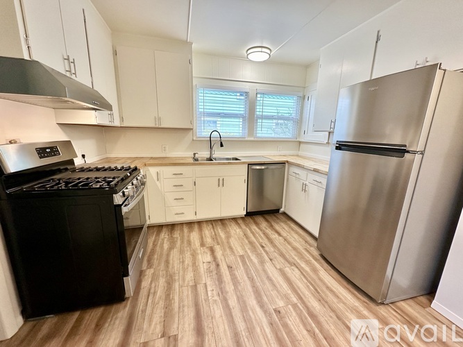 A kitchen with a black stove top oven, white cabinets, and a wooden floor.