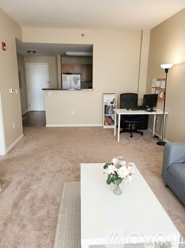 A living room with a white couch, a white coffee table with flowers, and a small desk with a computer.