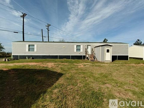 A grey house with a white door and windows is surrounded by a grassy area.