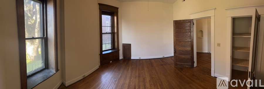 A room with wooden floors and white walls, with a large window on the left and a door on the right.