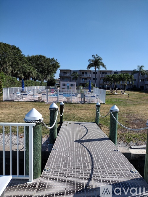 A wooden walkway leads to a white fence and a building in the background.