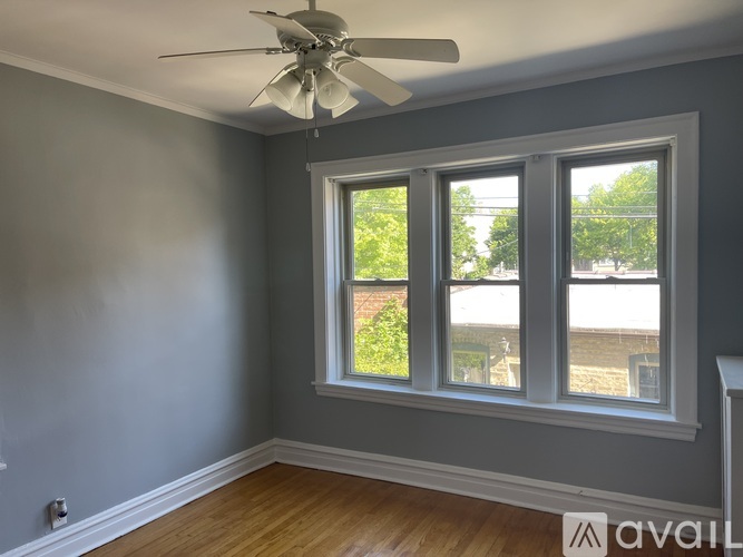 A room with a ceiling fan and a window with a view of a fence and trees.