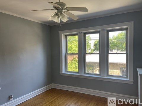A room with a ceiling fan and a window with a view of a fence and trees.