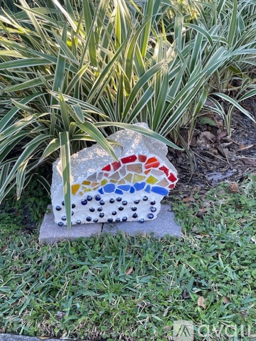 A small mosaic of a rainbow and dots is sitting on a stone.
