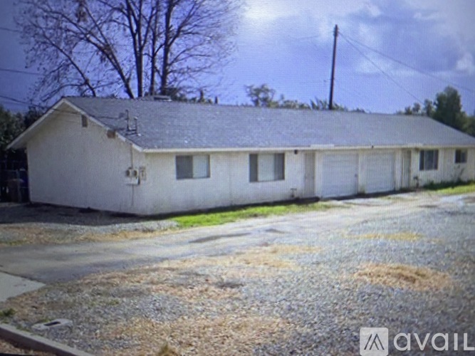 A white house with a grey roof is surrounded by a gravel driveway.