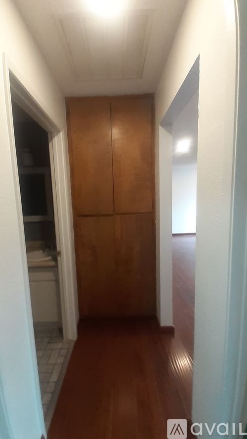 A hallway with a wooden floor and a cabinet on the left.
