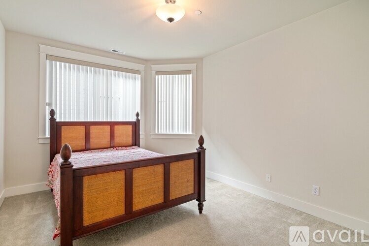 A bedroom with a bed, carpet, and two windows.