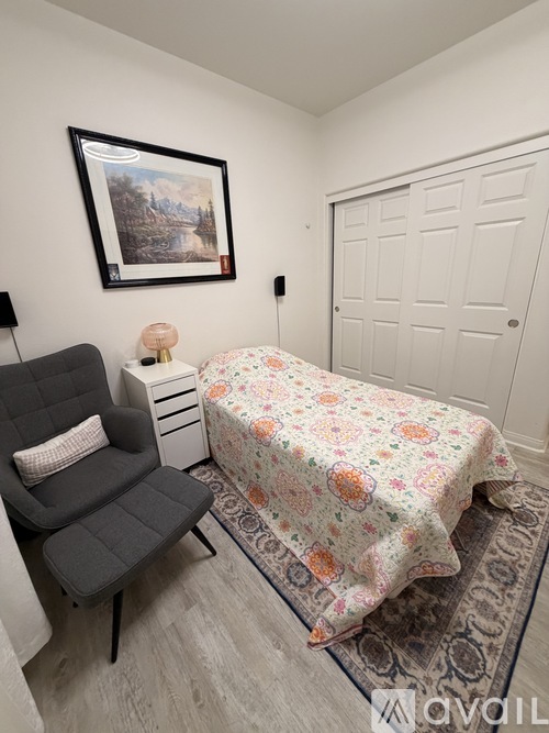 A bedroom with a floral bedspread and a grey chair.