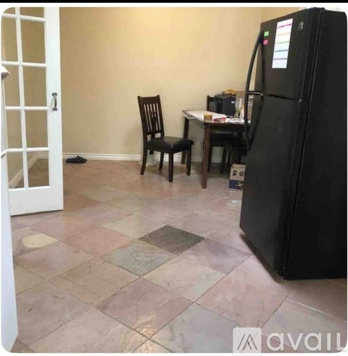 A black fridge is in a kitchen with a chair and table.