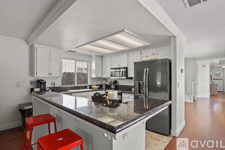 A kitchen with a red stool and a black fridge.